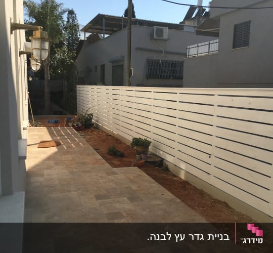 גדר עץ לבנה לצד שביל מרוצף בגינה